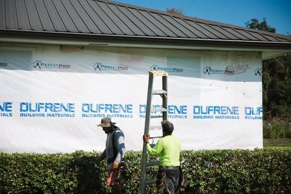Collins Construction crew working from a ladder on a house with branded wrap